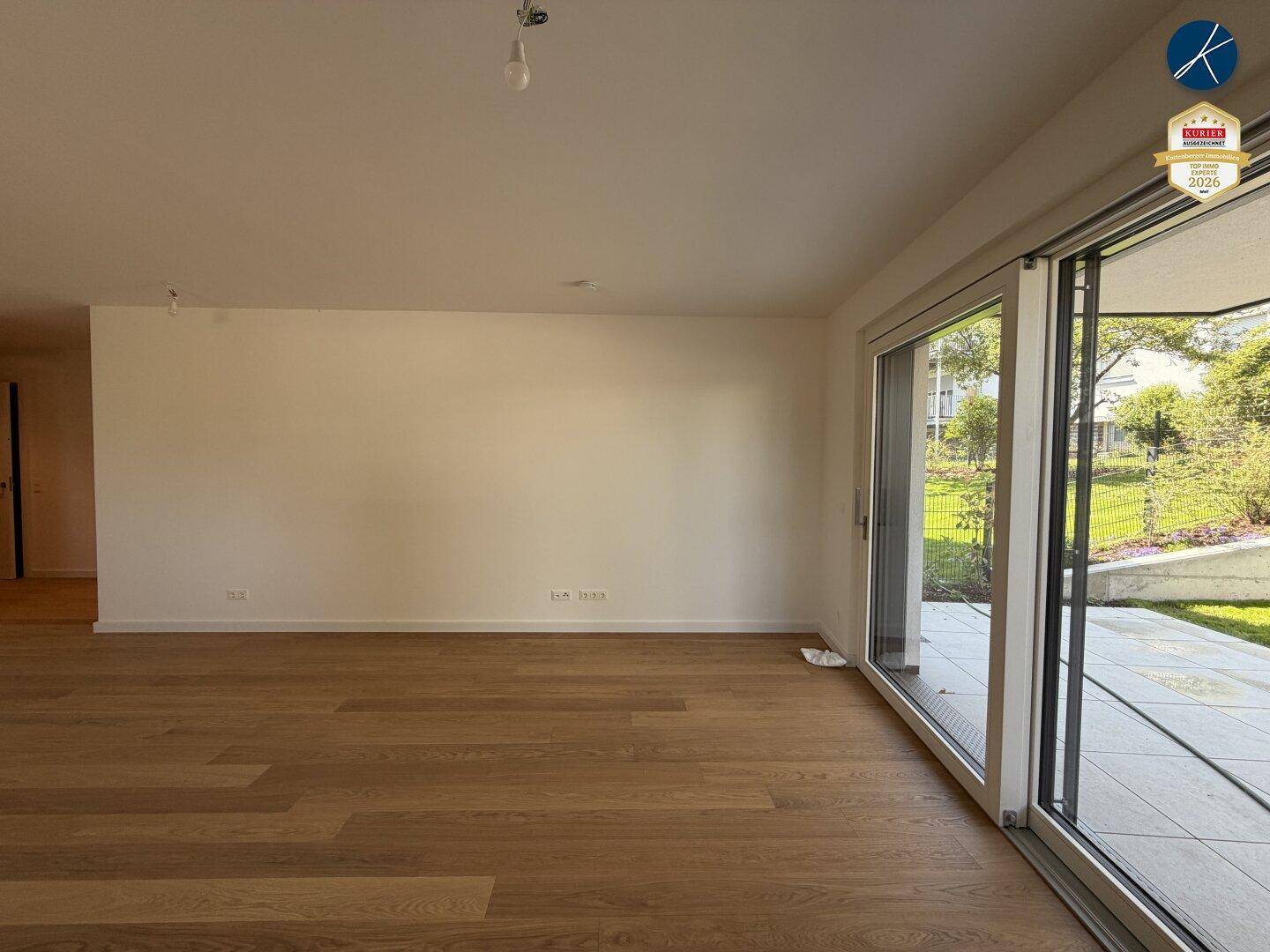 Heller, leerer Wohnbereich mit elegantem Holzboden und großen Schiebetüren zur Terrasse.