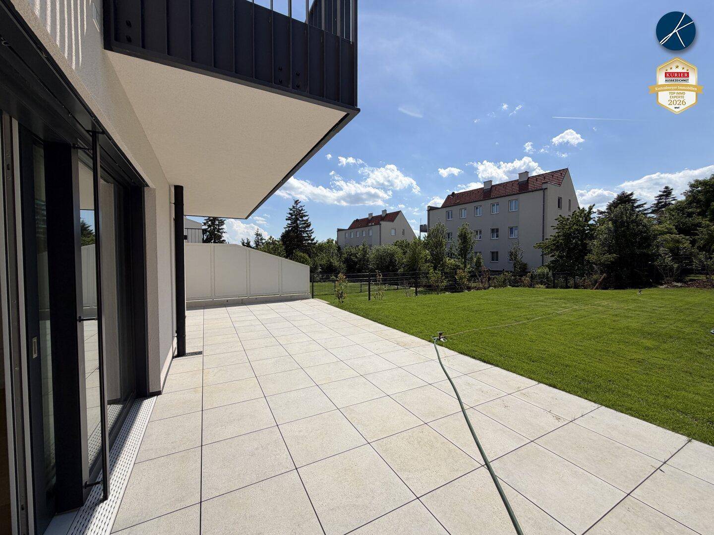 Weitläufige, geflieste Terrasse mit Blick auf den gepflegten Rasen und die umliegenden Gebäude.
