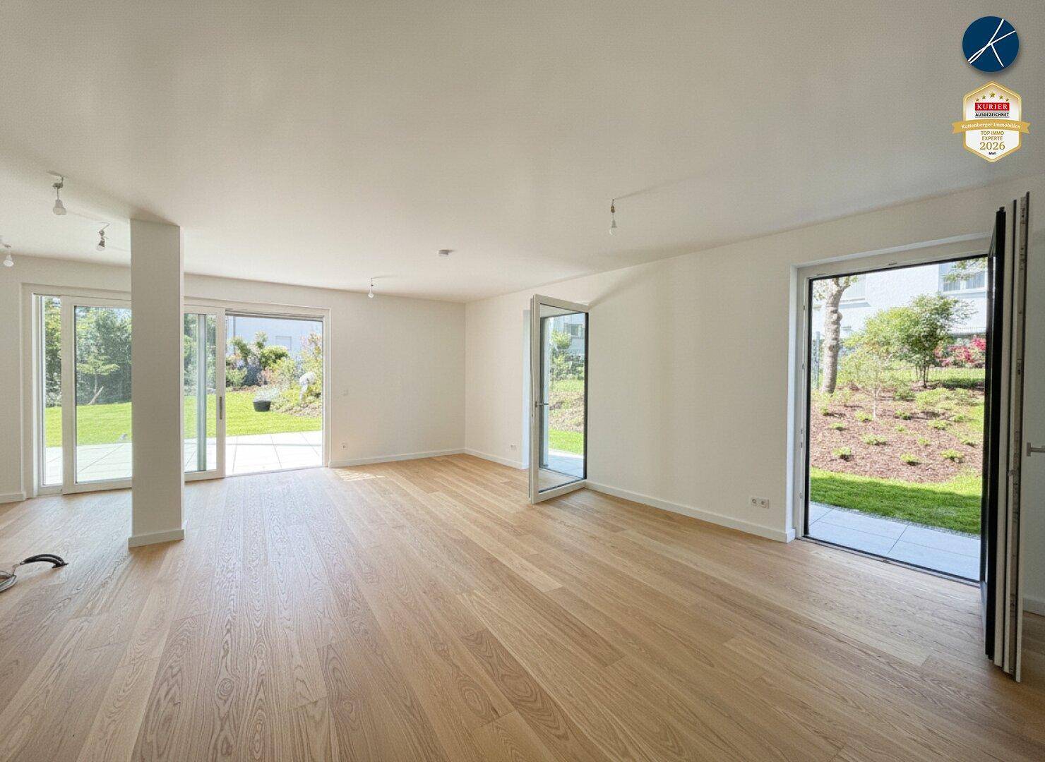 Geräumiges, leeres Wohnzimmer mit Holzboden und mehreren Zugängen zur Terrasse und zum Garten.