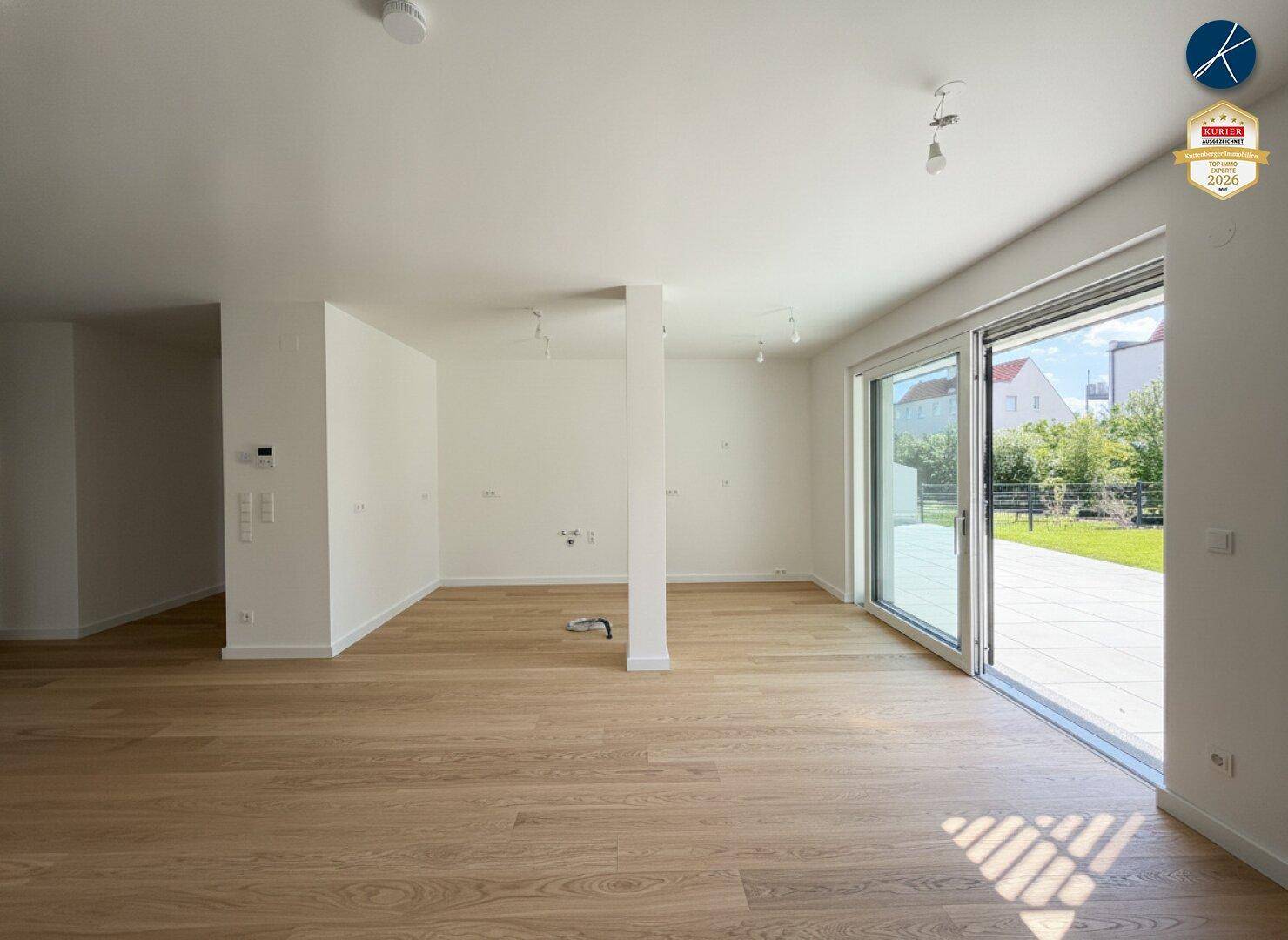 Heller, leerer Wohnbereich mit Holzboden und großer Schiebetür zur Terrasse und zum Garten.