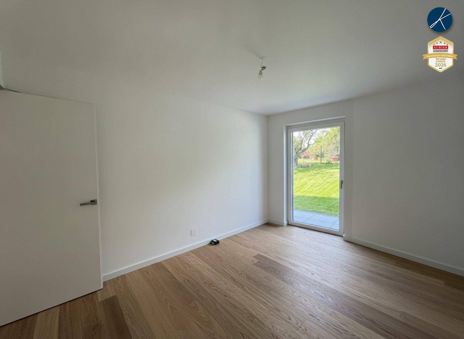 Helles, leeres Zimmer mit Holzboden und Blick ins Grüne, bereit für die Einrichtung.