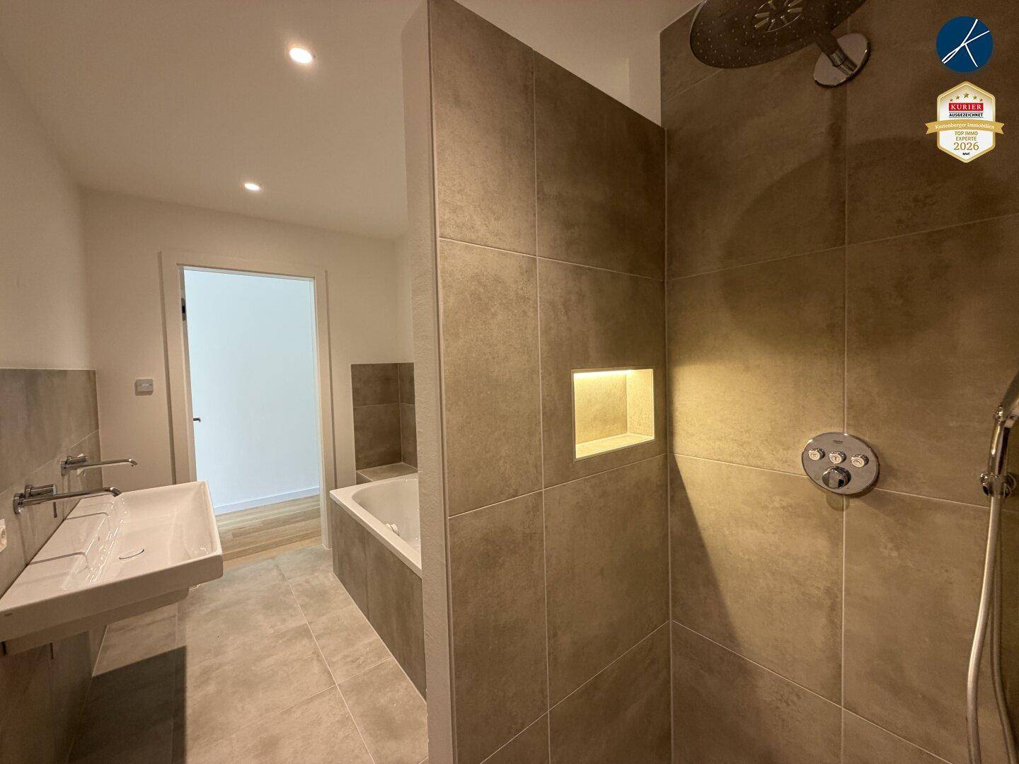 Modernes Badezimmer mit großformatigen Fliesen, begehbarer Dusche und integrierter Nische.