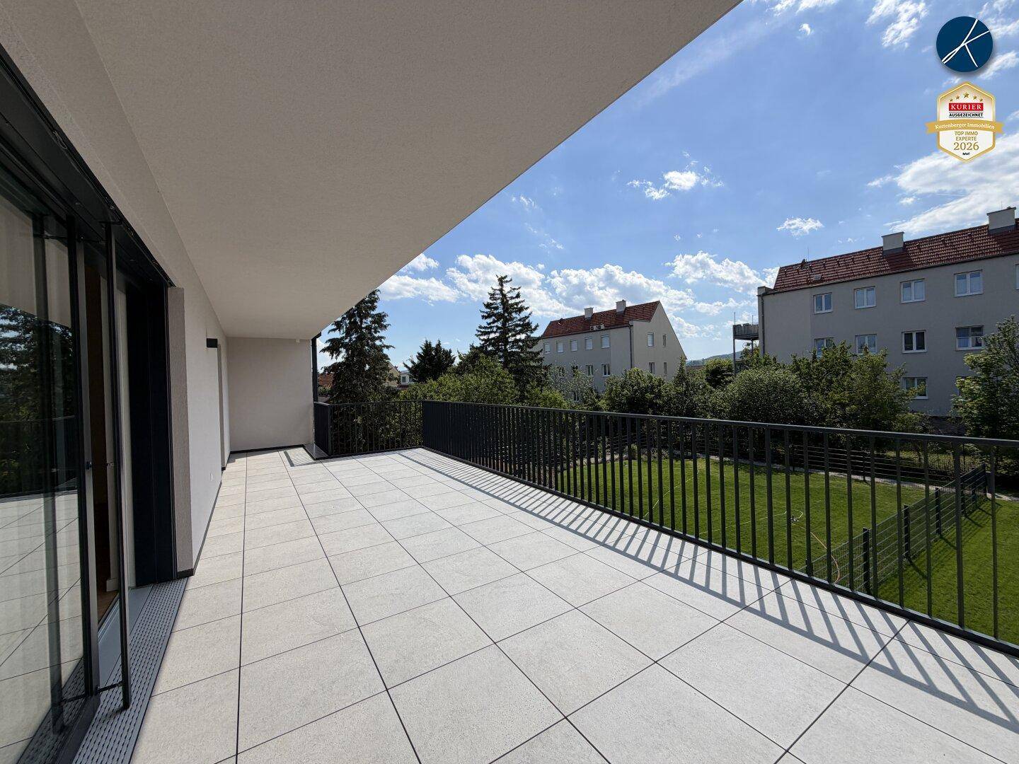 Geräumige, geflieste Terrasse mit Blick ins Grüne und auf umliegende Wohngebäude.
