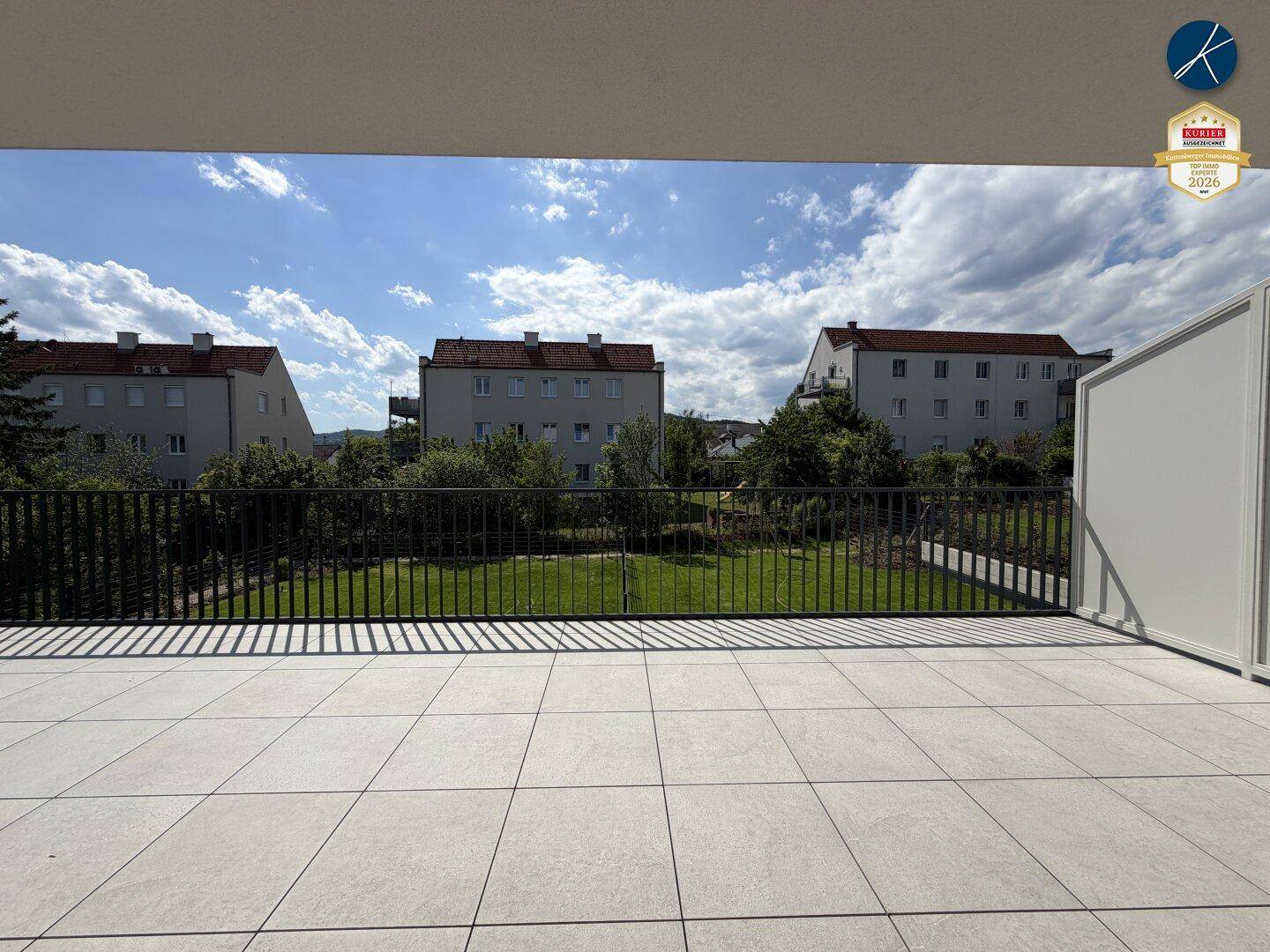Weitläufiger Blick von der Terrasse auf eine grüne Rasenfläche und Nachbargebäude.