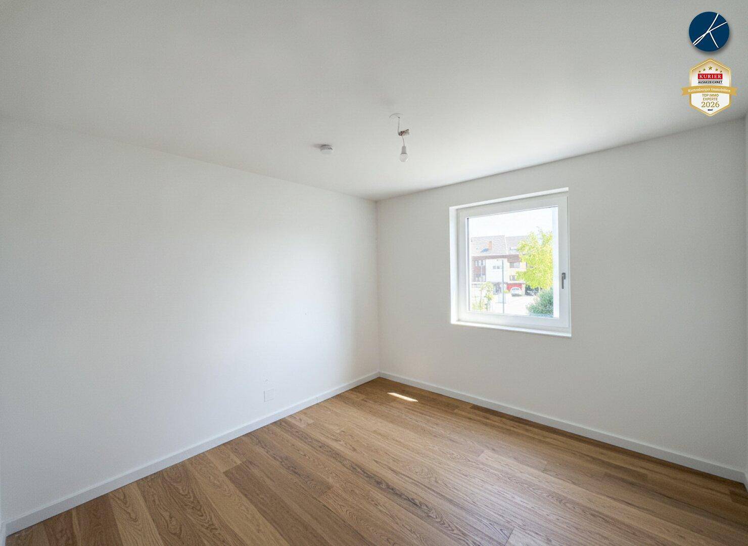 Helles Zimmer mit Parkettboden und Blick ins Grüne durch das Fenster.