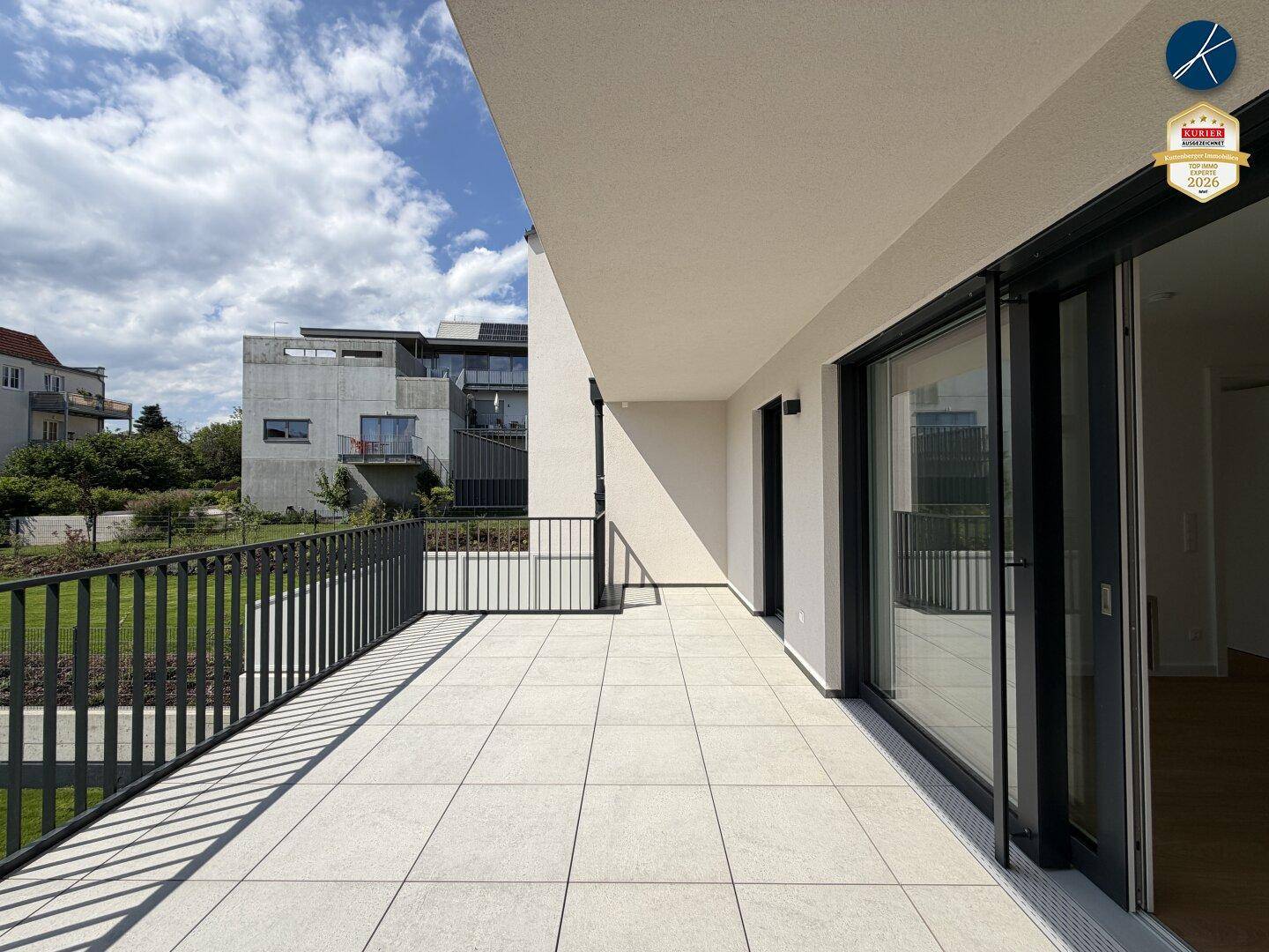 Weitläufige, geflieste Terrasse mit modernem Geländer und Blick auf die umliegende Bebauung.