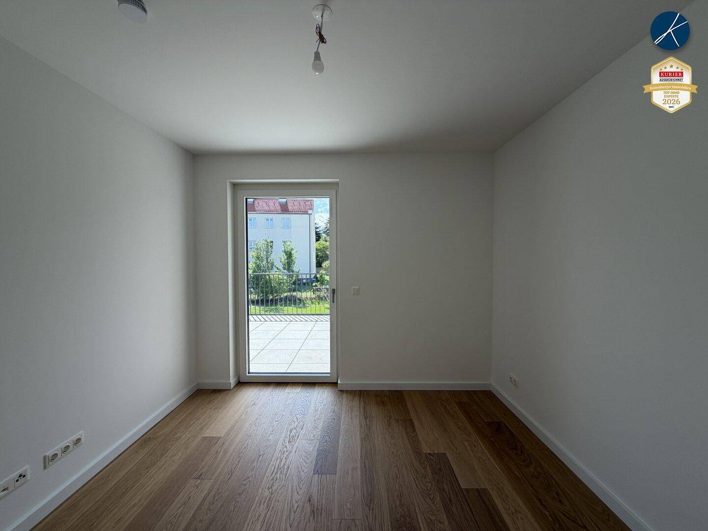 Helles Zimmer mit Holzboden und Zugang zu einem Balkon, ideal als Schlafzimmer.