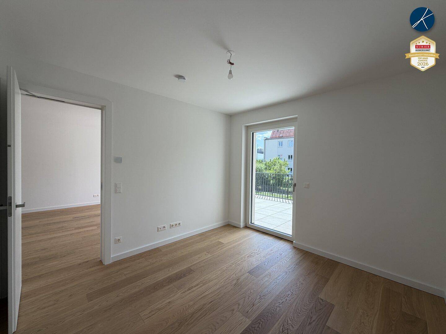Leeres Zimmer mit Holzboden und Balkonzugang, bereit für individuelle Gestaltung.
