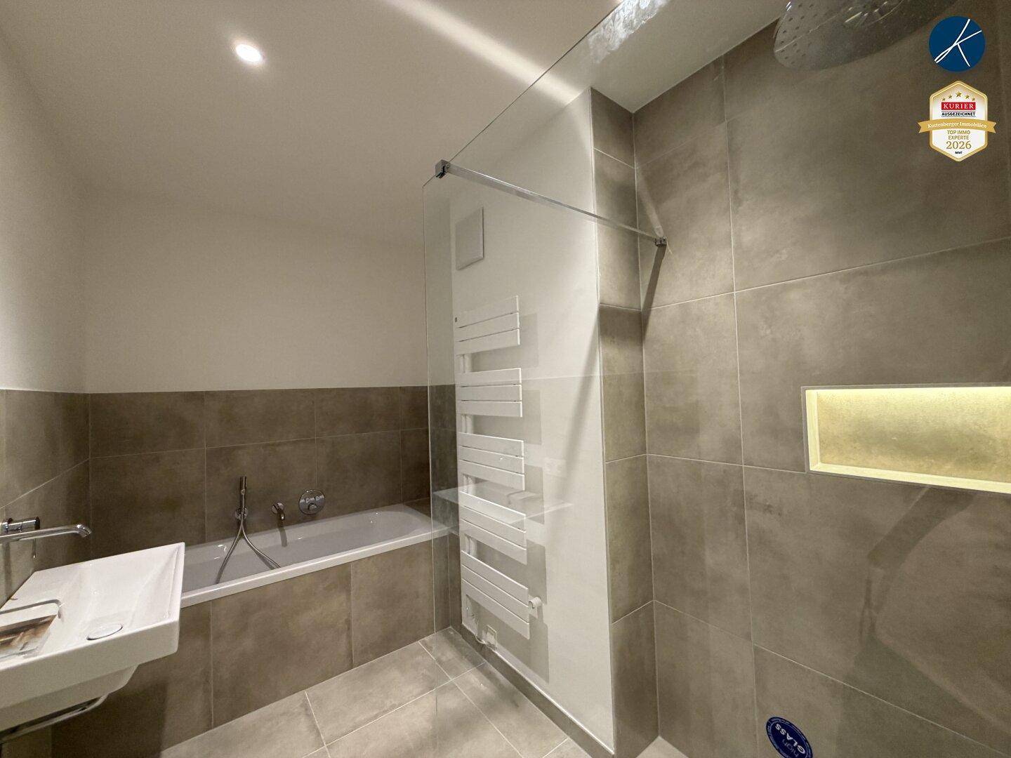 Modernes Badezimmer mit Badewanne, Duschbereich und beheiztem Handtuchhalter.