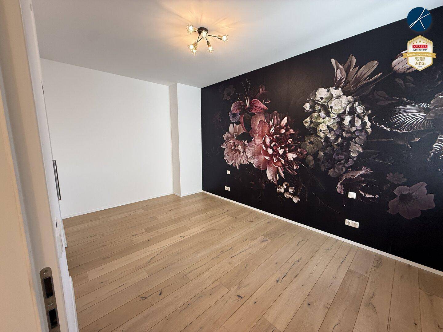 Schlafzimmer mit hellem Parkettboden und einer auffälligen Wand mit dunkler floraler Tapete.