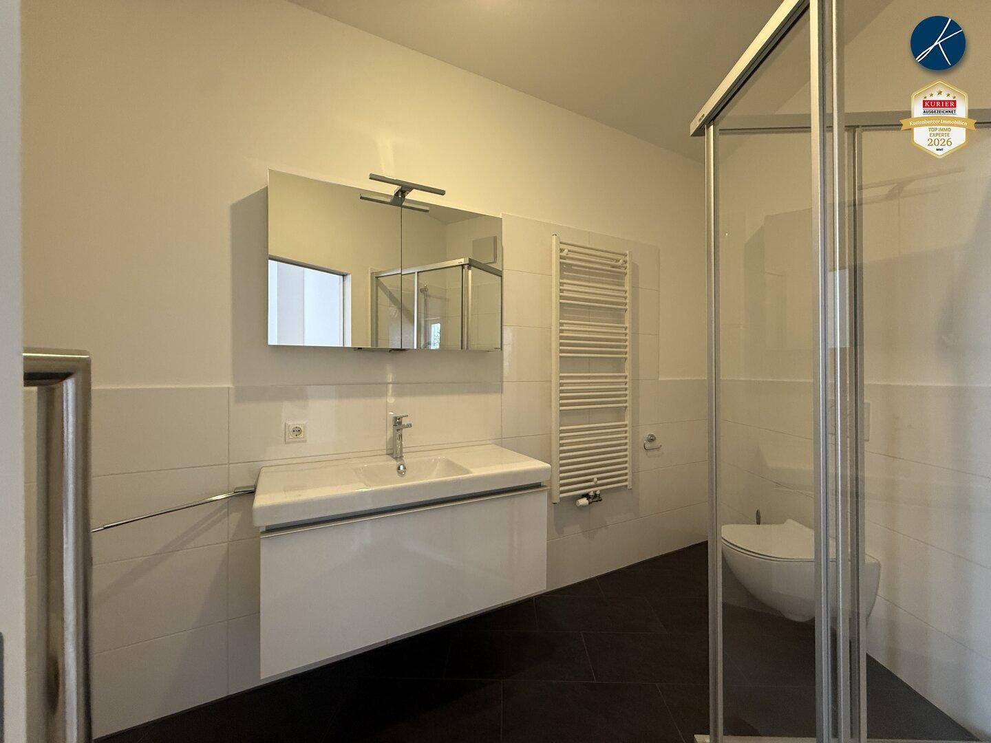 Modernes Badezimmer mit Doppelwaschbecken, Duschkabine, Wand-WC und beheiztem Handtuchhalter.