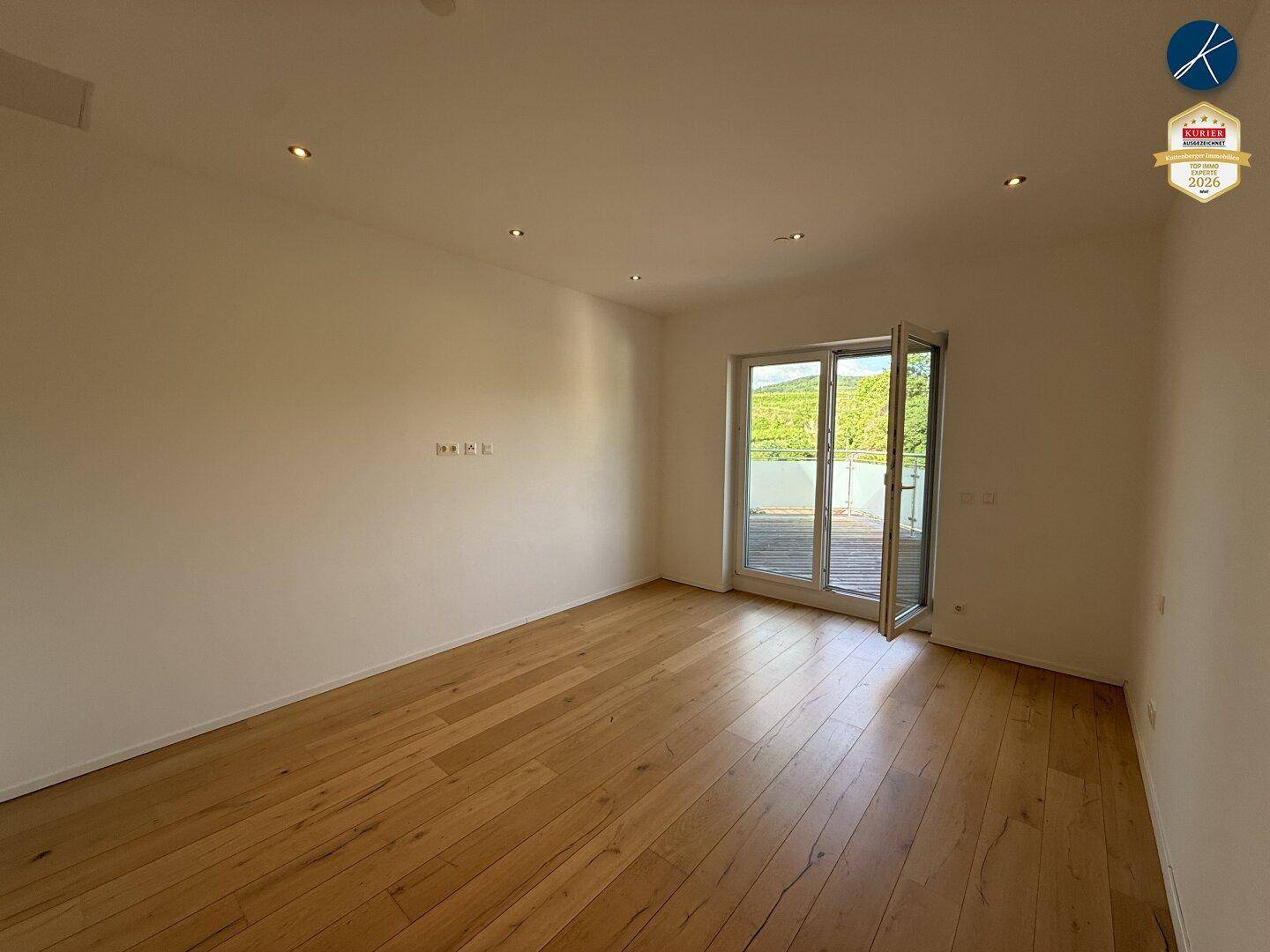 Helles Zimmer mit Parkettboden und Zugang zu einem Außenbereich mit weitem Grünblick.