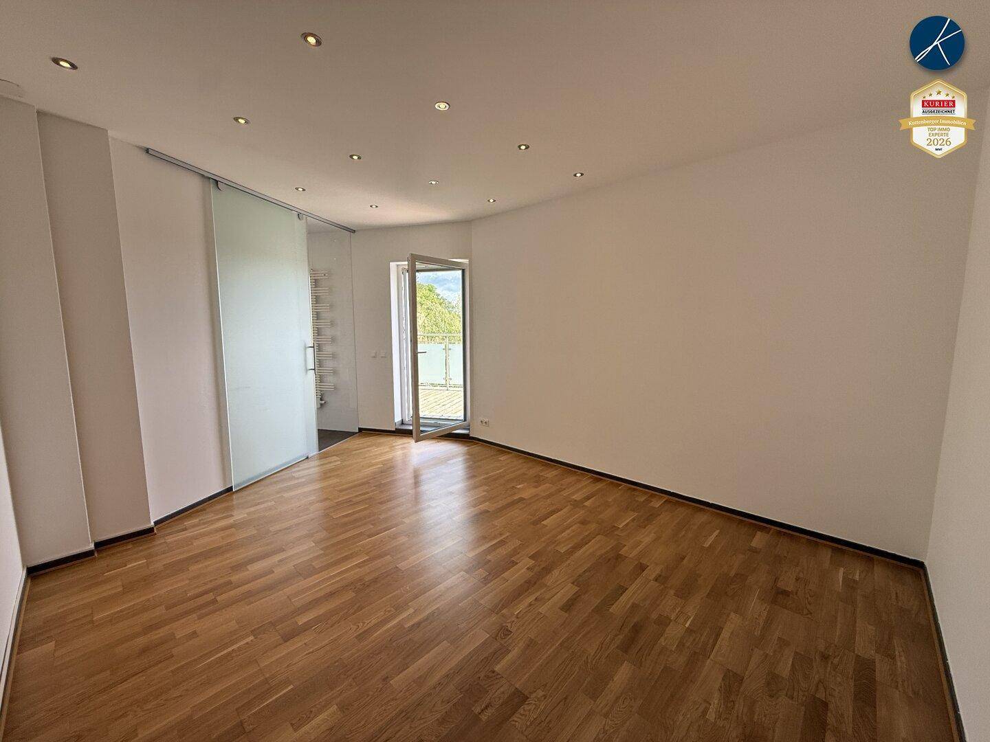 Helles Zimmer mit Parkettboden und Glasschiebetür, die zu einem sonnigen Außenbereich führt.