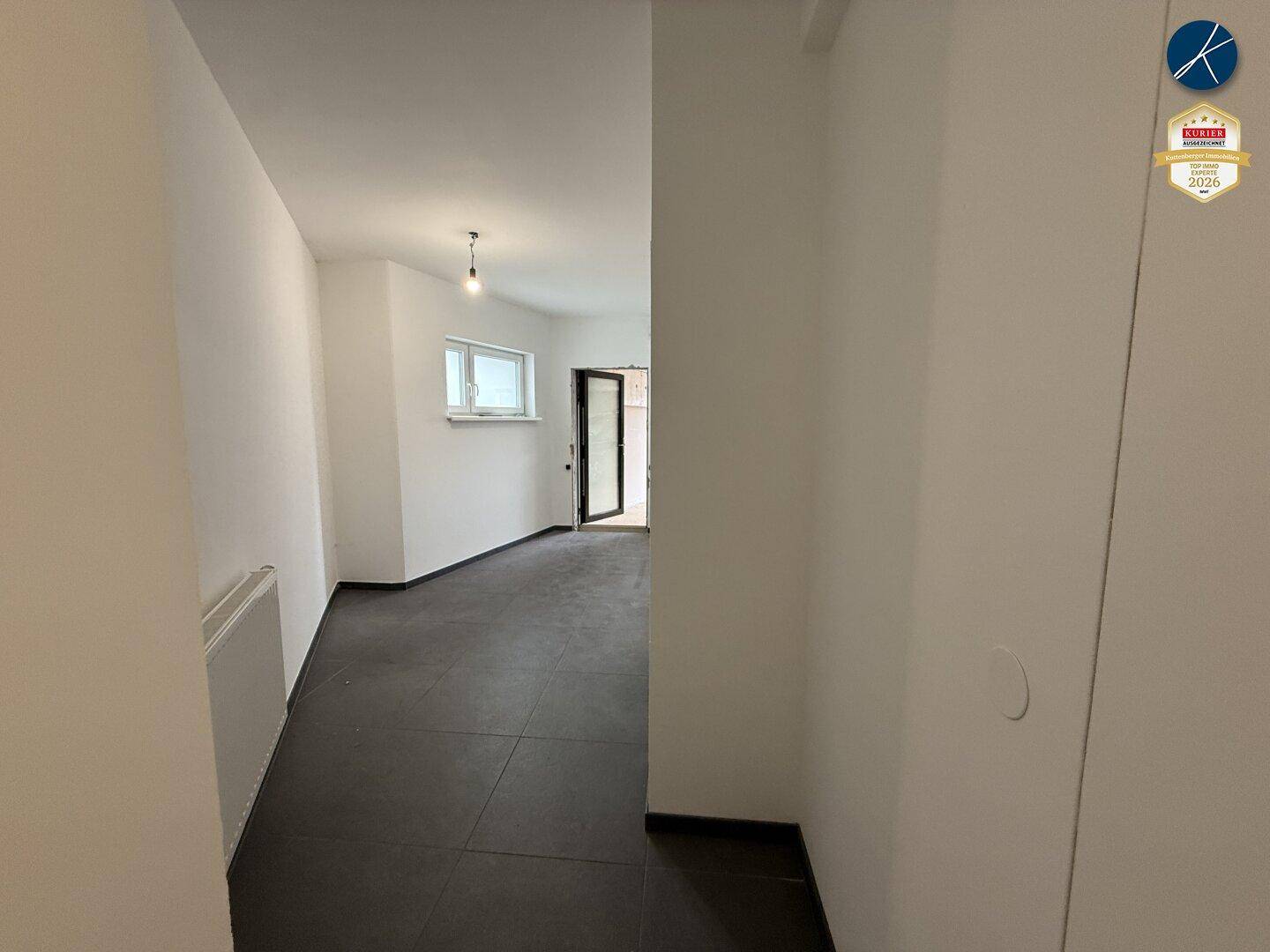 Heller Flur mit dunklem Fliesenboden, weißen Wänden und einem Fenster für natürliches Licht.