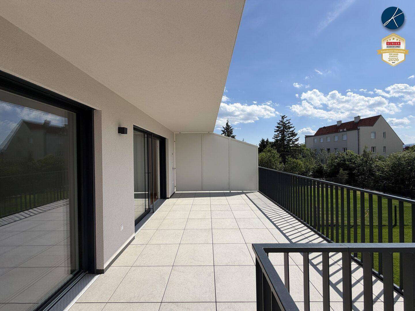 Große, geflieste Terrasse mit schwarzem Geländer und Blick auf die Umgebung unter blauem Himmel.
