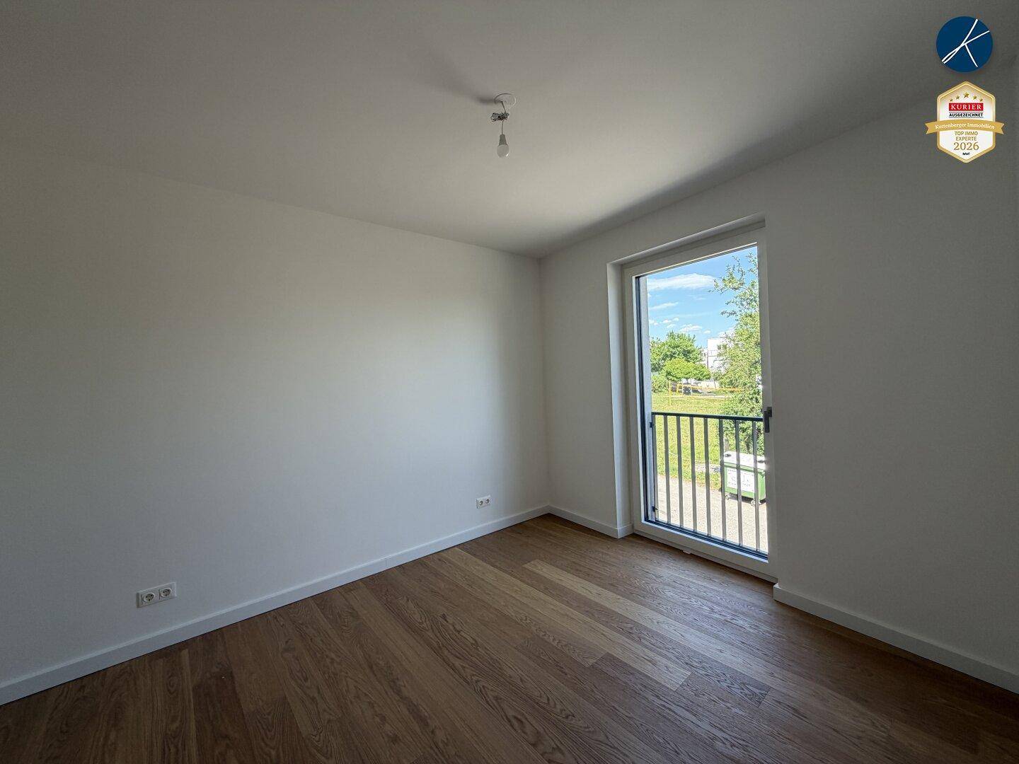Helles Schlafzimmer mit Parkettboden und großem Fenster mit Blick ins Grüne.