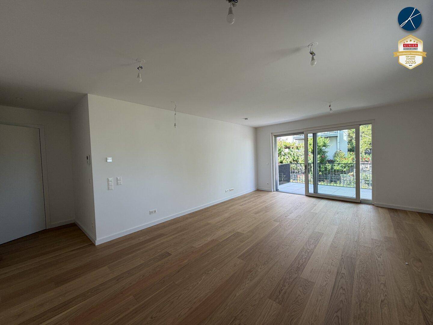 Großzügiges Wohnzimmer mit hellem Parkettboden und Zugang zu einem Balkon.