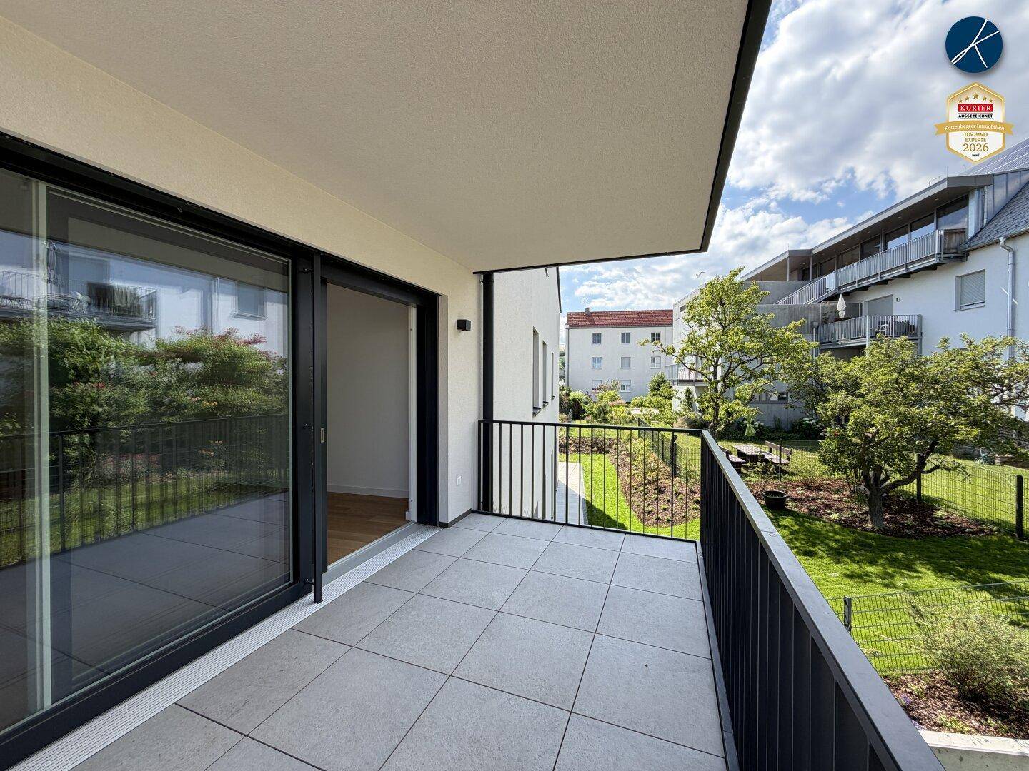 Heller Balkon mit Fliesenboden und Blick auf den begrünten Innenhof der Wohnanlage.