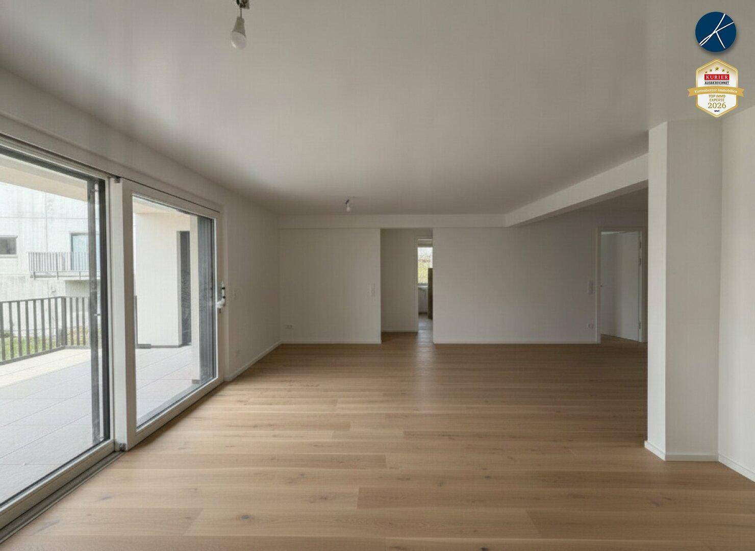 Geräumiges, leeres Wohnzimmer mit hellem Holzparkett und Zugang zu einem großen Balkon.