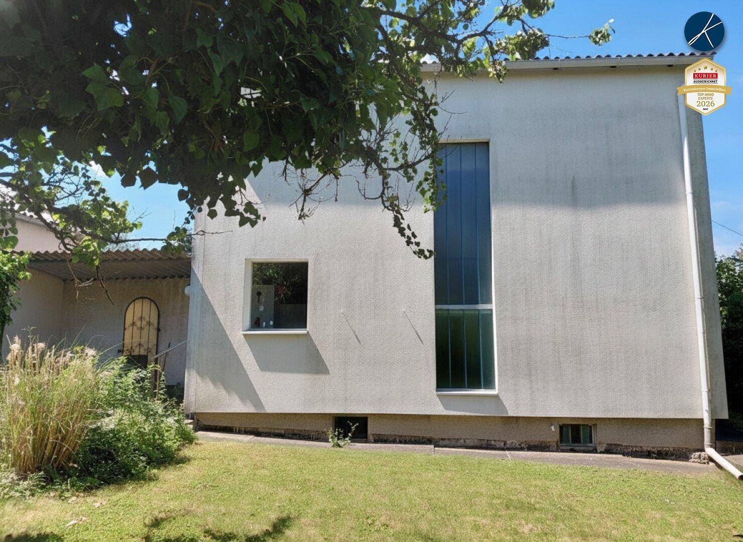 Rückseite des Hauses mit großen Fenstern und Zugang zum grünen Gartenbereich.