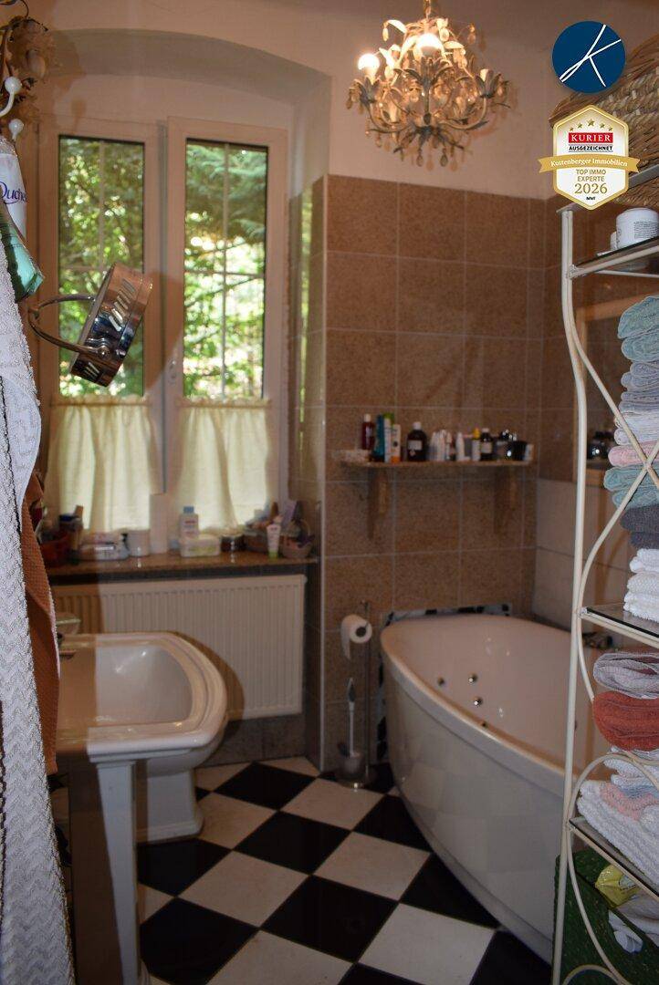 Badezimmer mit Eckbadewanne, Schachbrettfliesen und Fenster mit Blick ins Grüne.