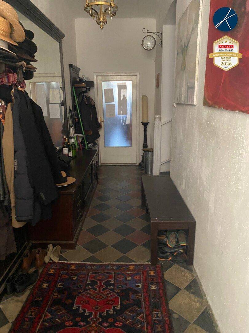 Langer Flur mit gemusterten Fliesen, Garderobe und antiken Möbeln.