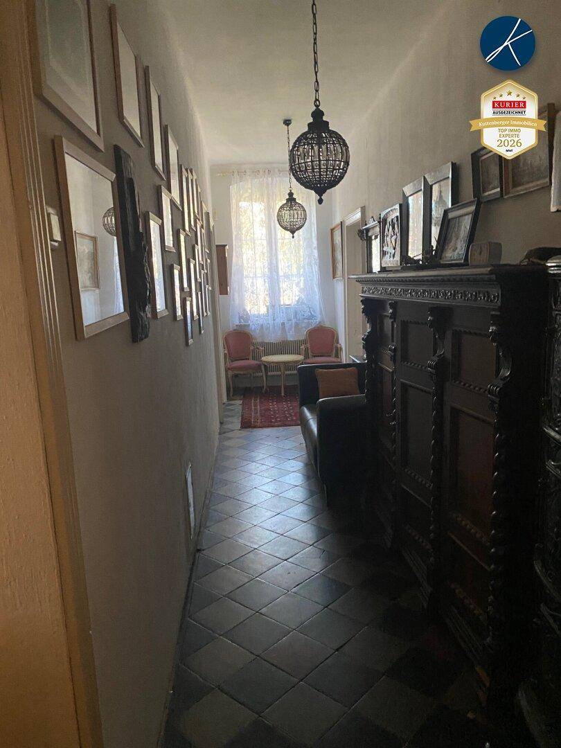 Langer Flur mit vielen gerahmten Bildern, dunklen Fliesen und Sitzgelegenheiten am Ende.