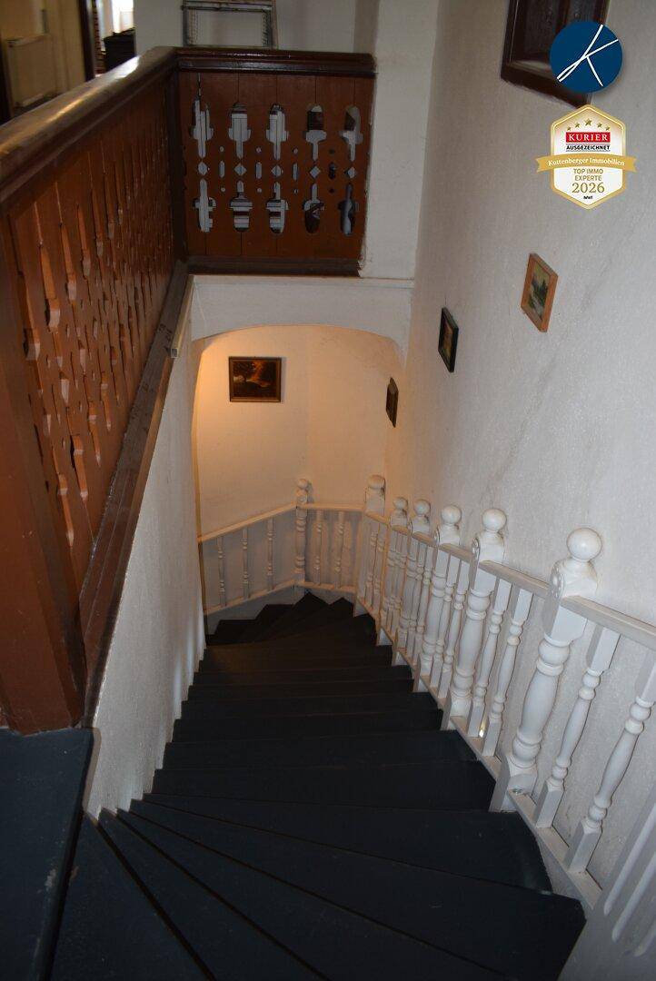 Treppenhaus mit Holzgeländer und dunklen Stufen, das die verschiedenen Etagen verbindet.