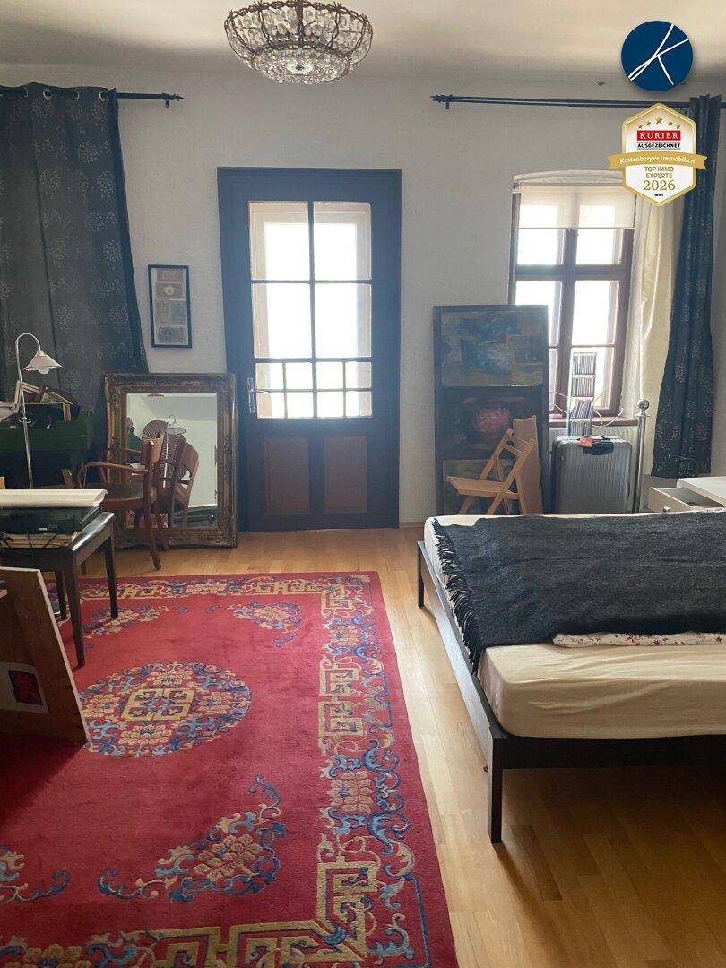 Helles Schlafzimmer mit Holzboden, großem Teppich und Zugang zu einem Balkon oder Terrasse.
