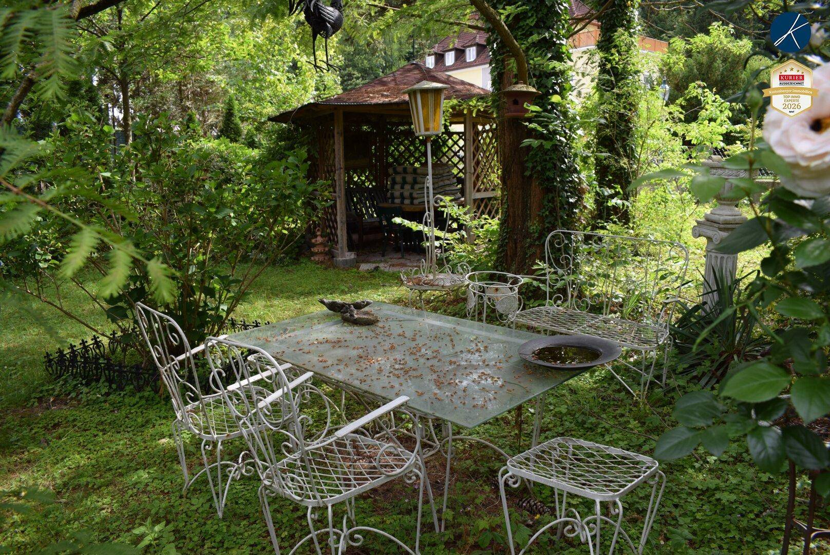 Idyllischer Gartenbereich mit Gartenmöbeln, Laube und üppiger Vegetation.