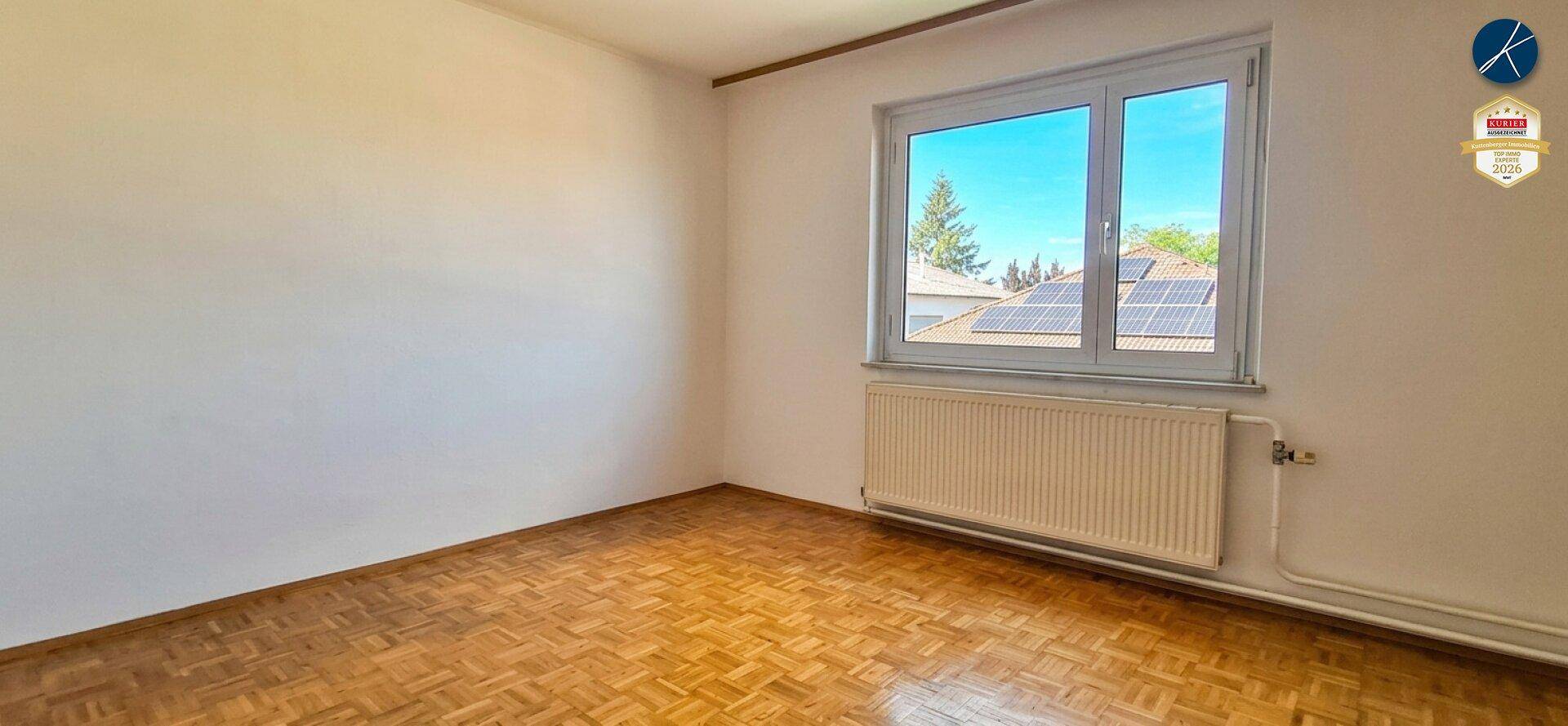 Geräumiges Zimmer mit Parkettboden, weißen Wänden und weitem Blick aus dem Fenster.