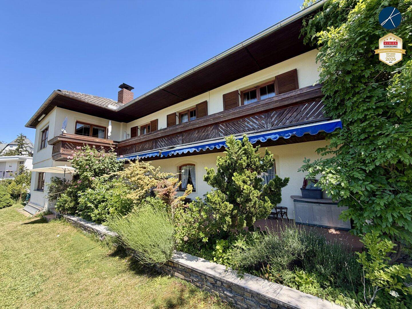 Seitenansicht des Hauses mit Balkon, Terrasse und üppiger Bepflanzung im Garten.