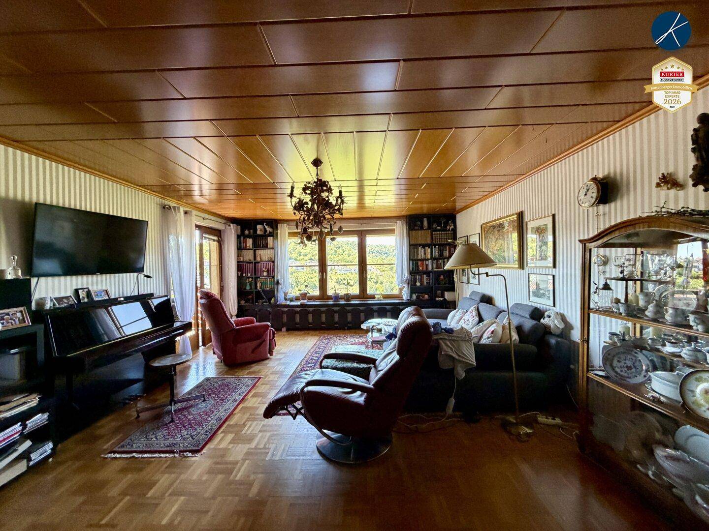 Geräumiges Wohnzimmer mit Parkettboden, Holzdecke und großem Fenster mit Weitblick.