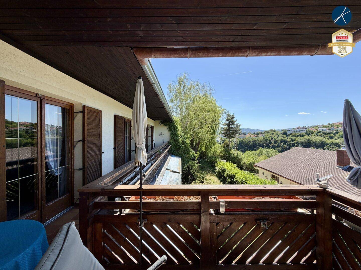 Großer Holzbalkon mit Sitzgelegenheiten und Panoramablick auf die grüne Umgebung.