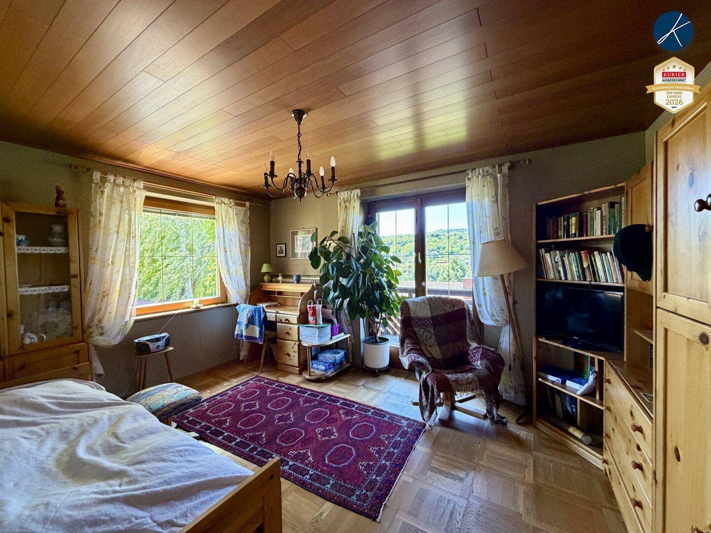 Schlafzimmer mit Holzboden, Holzdecke, Schreibtisch und Blick ins Grüne.
