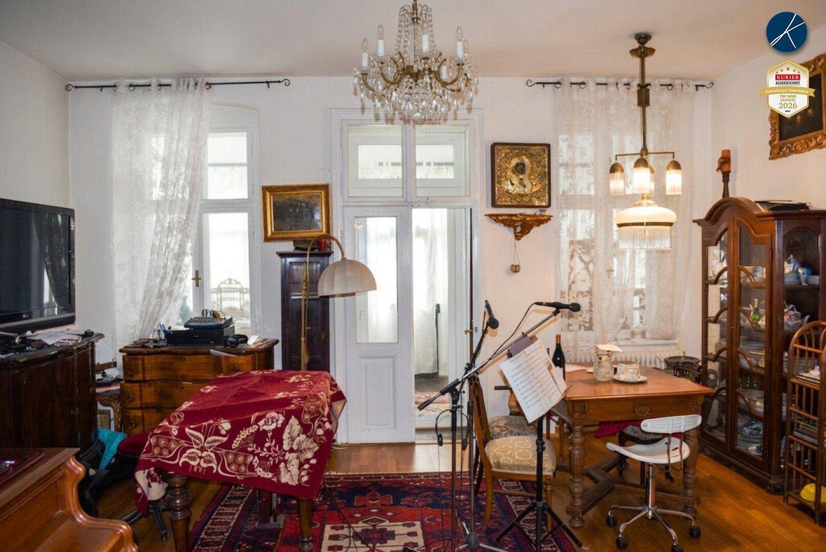 Geräumiges Wohnzimmer mit Kronleuchter, Holzboden und antiken Möbeln, ideal für Musikliebhaber.