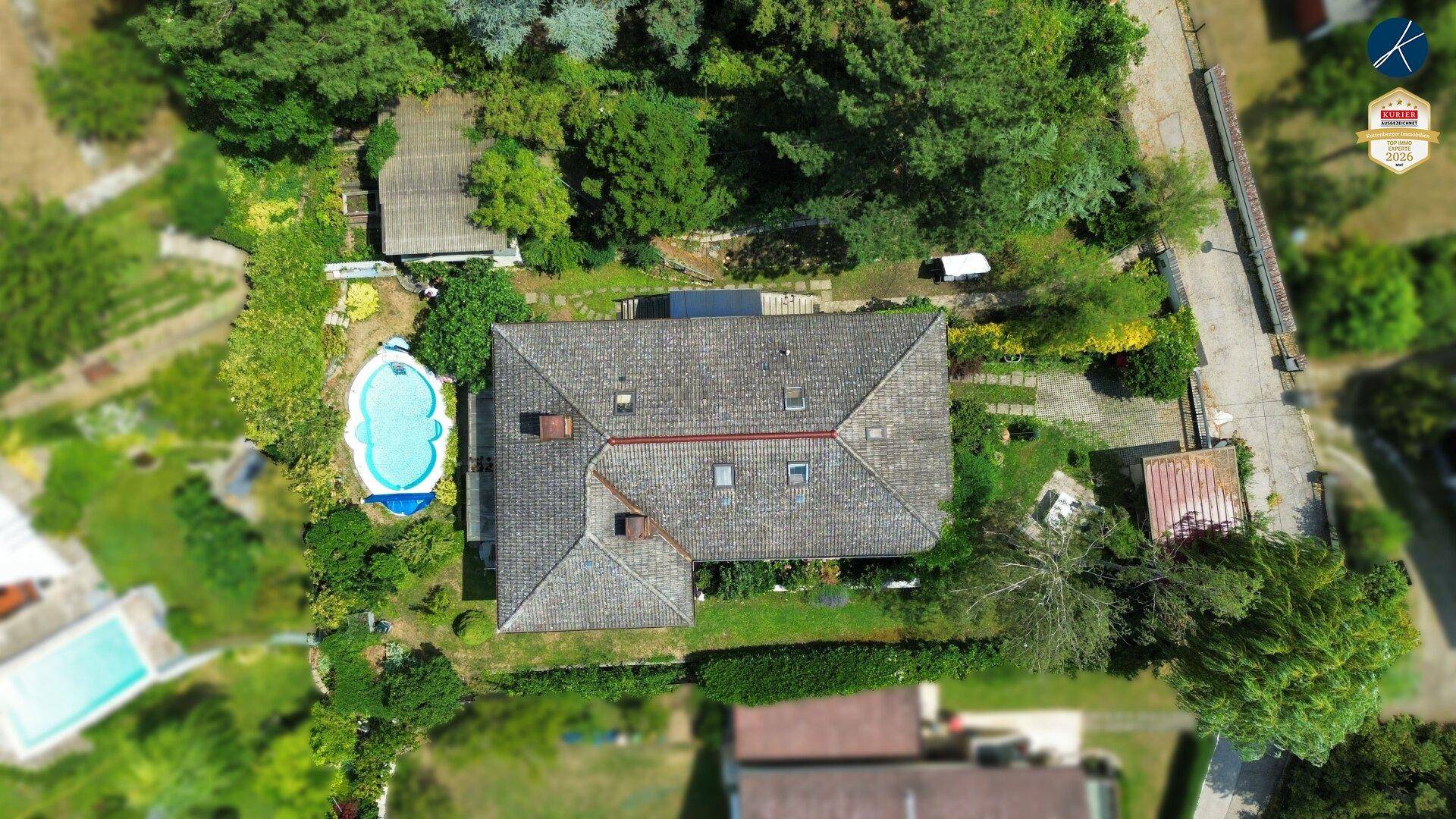 Vogelperspektive des Anwesens mit Haus, Garten, Pool und angrenzender Straße.