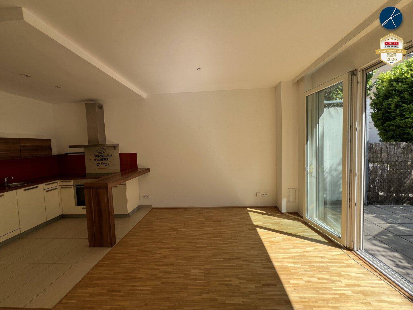 Heller offener Wohnbereich mit Parkettboden, integrierter Küche und Zugang zur Terrasse.