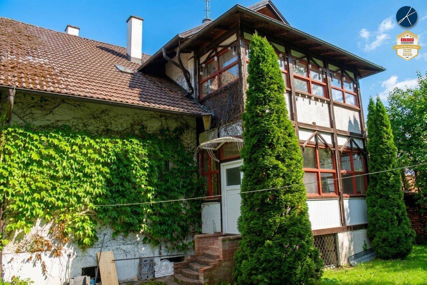 Historisches Gebäude mit bewachsenen Fassaden und hohen Bäumen im Garten.