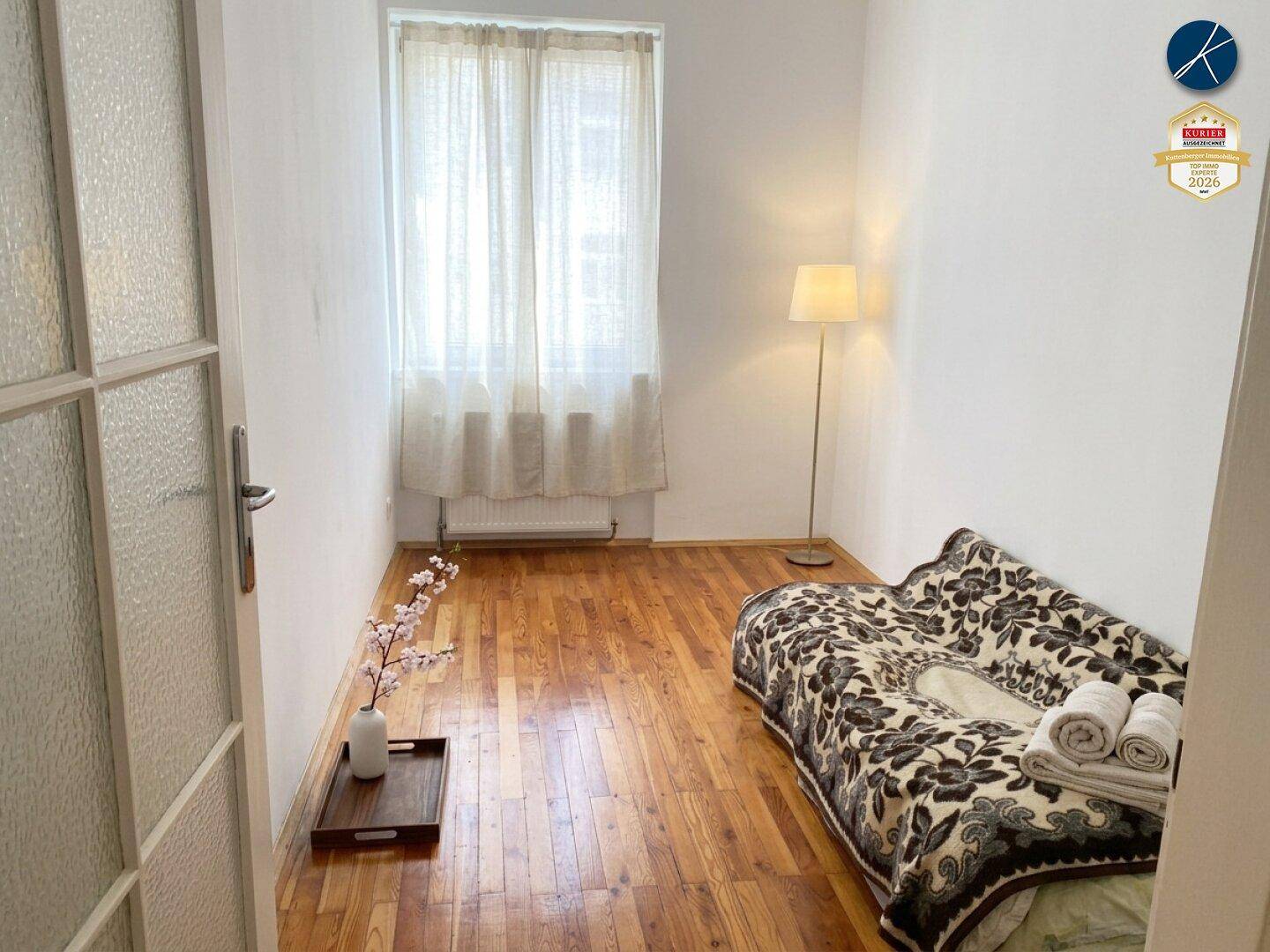 Gemütliches Schlafzimmer mit Holzboden, einem Fenster und einfacher Einrichtung, ideal als Gästezimmer.