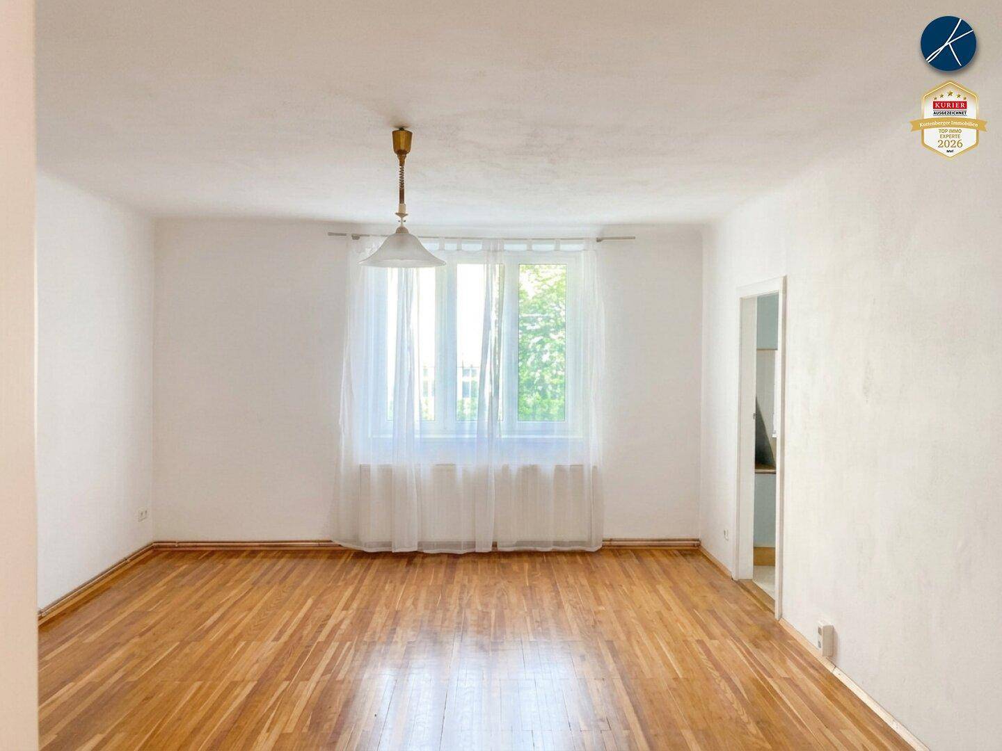 Helles Wohnzimmer mit glänzendem Parkettboden und einem großen Fenster, das viel Tageslicht hereinlässt.