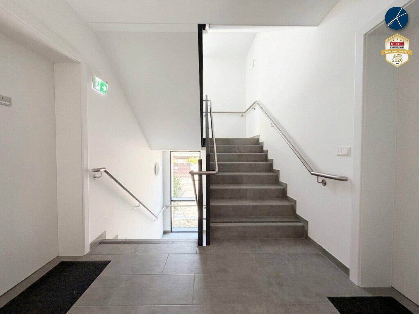 Modernes Treppenhaus mit hellen Stufen und Edelstahlgeländer.