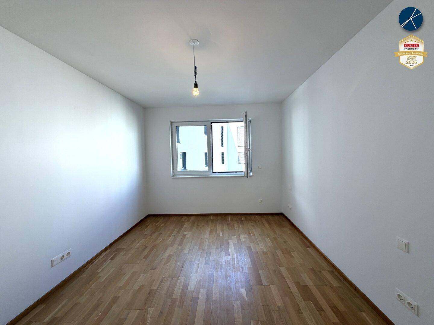 Helles Schlafzimmer mit Parkettboden und einem Fenster, das viel Tageslicht hereinlässt.