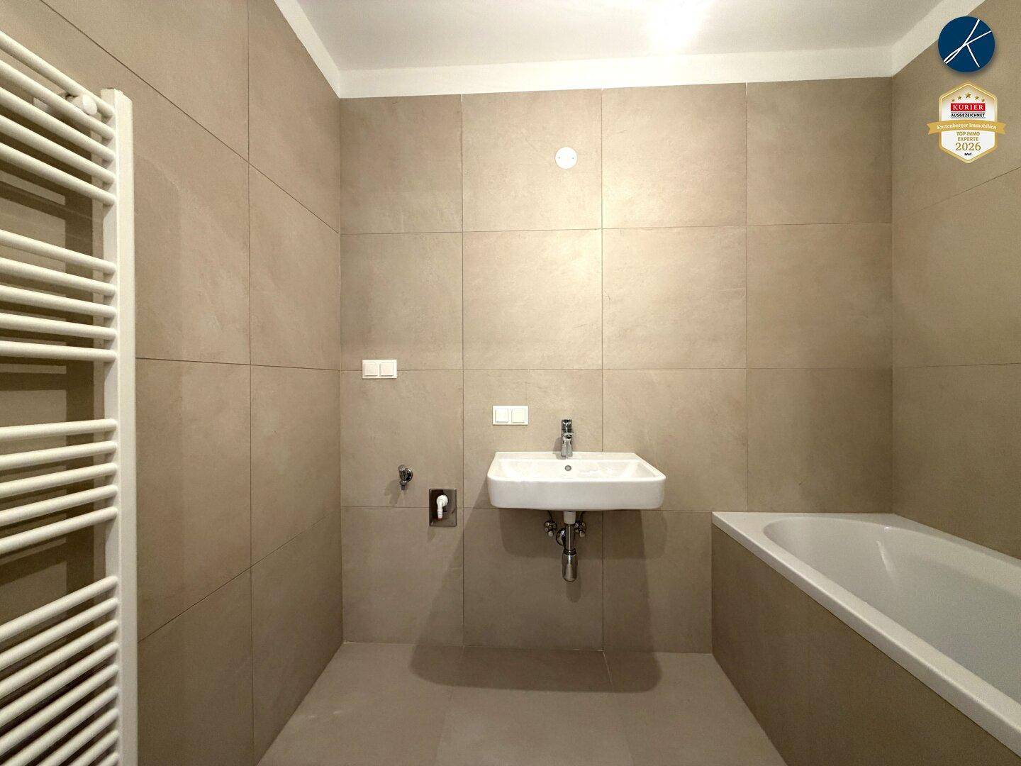 Modernes Badezimmer mit beigefarbenen Fliesen, Waschbecken, Badewanne und Handtuchheizkörper.