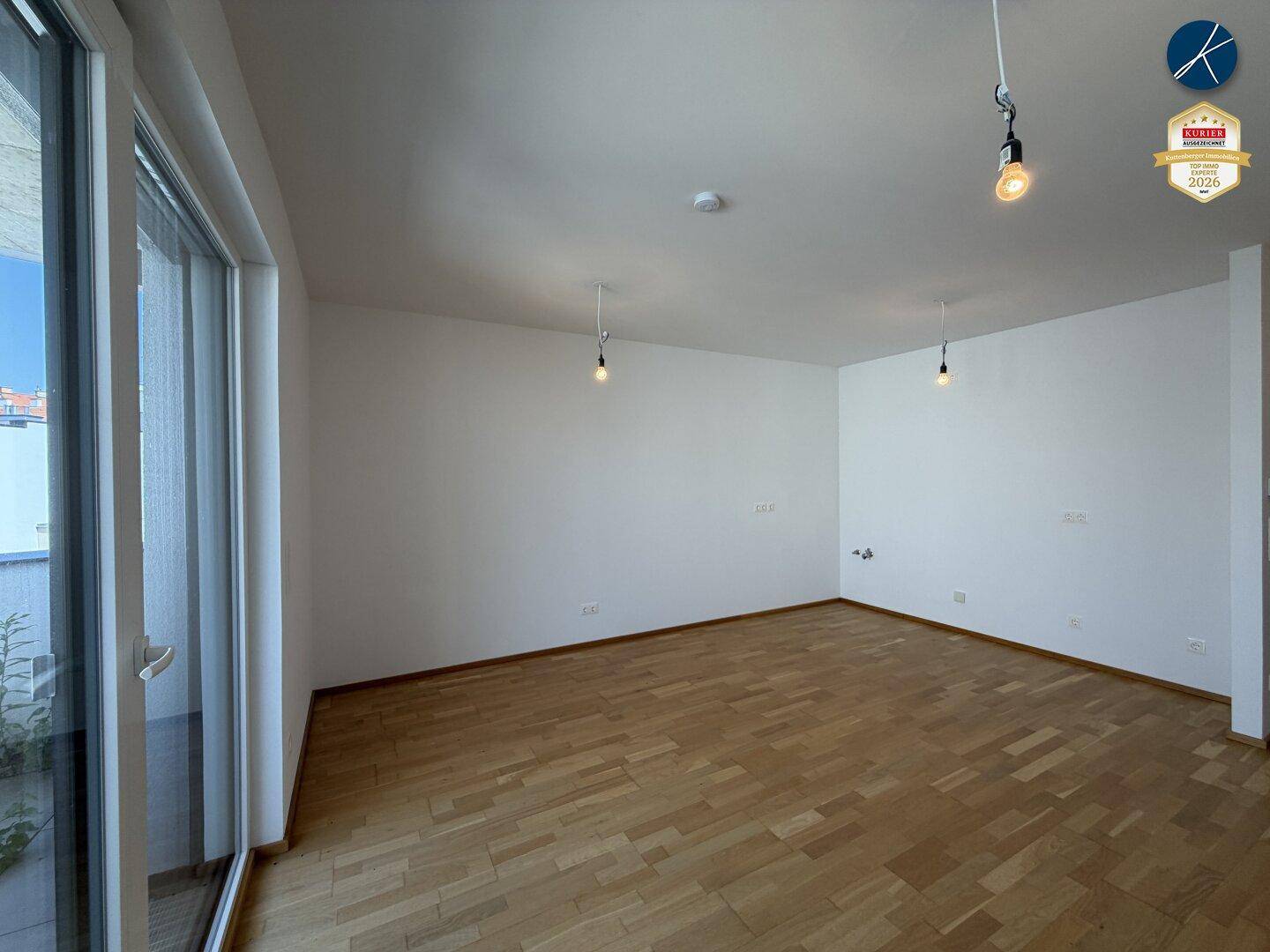 Lichtdurchflutetes Wohnzimmer mit Parkettboden und großen Fenstern.