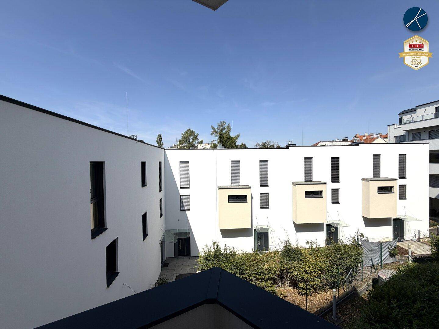 Blick auf die moderne Gebäudefassade mit mehreren Fenstern und einem begrünten Innenhof.