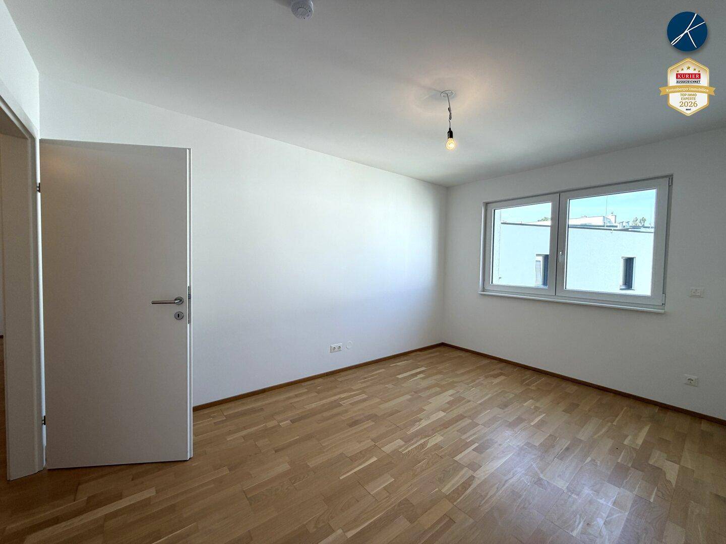 Helles Schlafzimmer mit Parkettboden und einem großen Fenster.