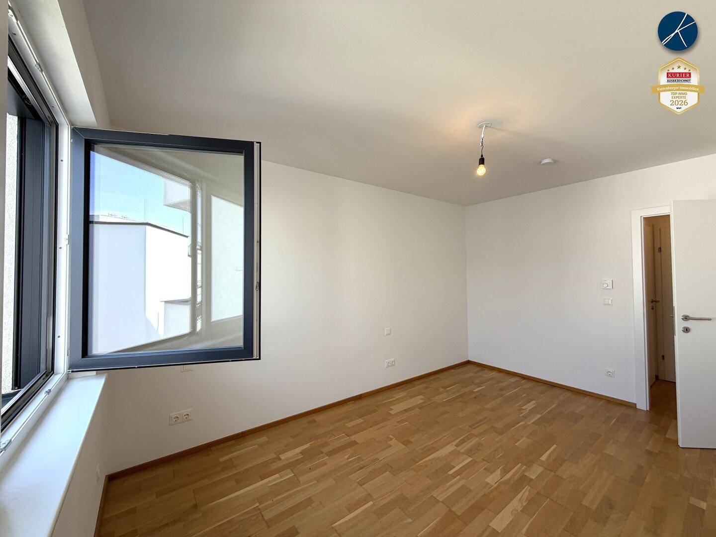 Schlafzimmer mit Parkettboden und einem geöffneten Fenster, das viel Licht hereinlässt.