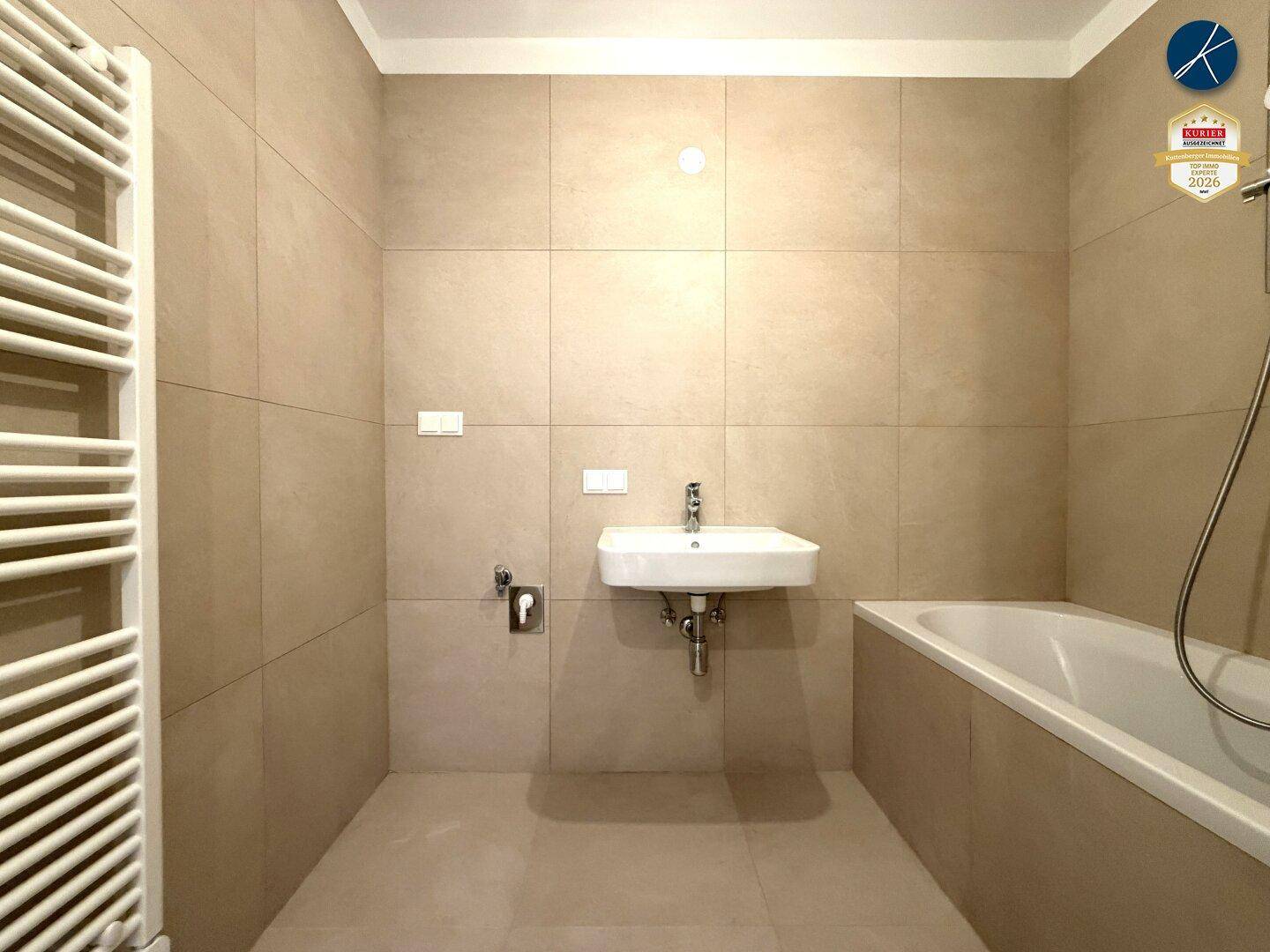 Modernes Badezimmer mit beigefarbenen Fliesen, Badewanne und Handtuchheizkörper.