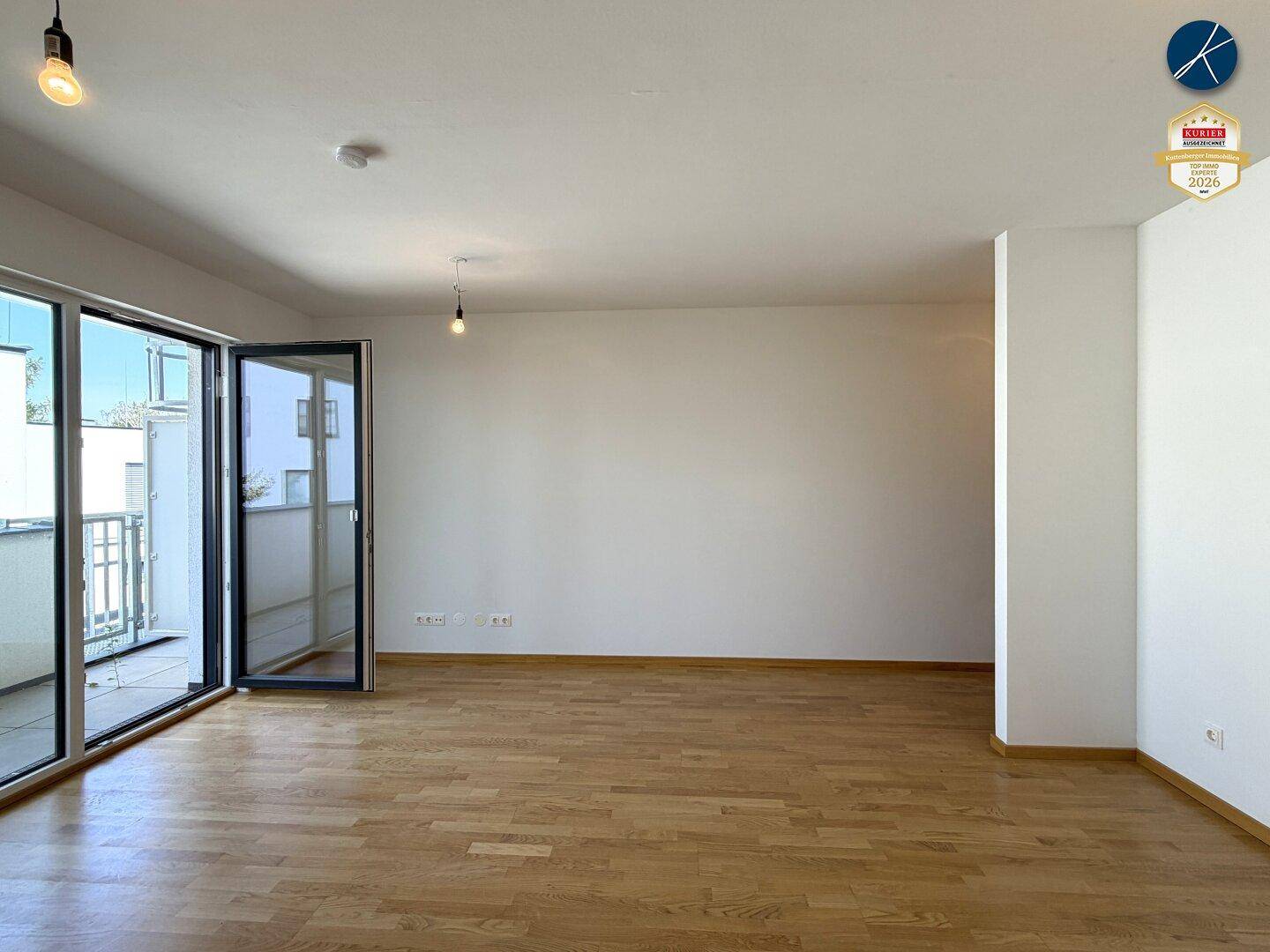 Heller Wohnbereich mit Parkettboden und großen Fenstertüren, die viel Tageslicht hereinlassen.